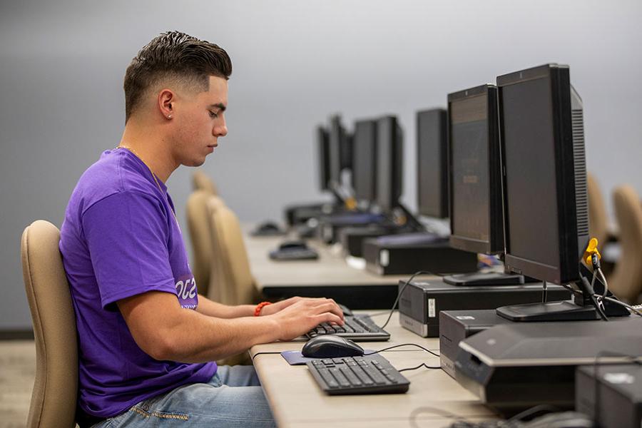 An individual wearing a purple shirt sits at a computer, typing on the keyboard